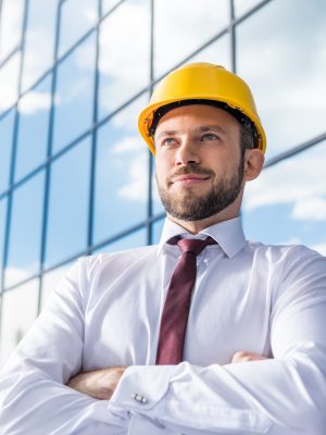portrait of smiling professional architect in hard hat against building