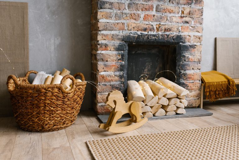 Red brick fireplace with firewood and a basket of firewood near it, children's wooden toy horse
